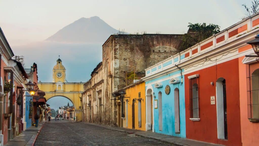 A vibrant street scene in Antigua Guatemala with colorful colonial buildings and a distant volcano i.