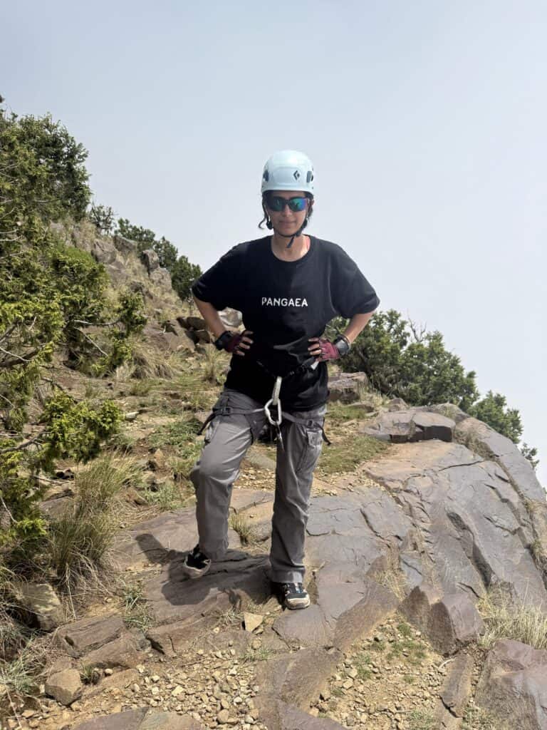 Woman hiking on rocky trail with helmet and sunglasses in outdoor mountain setting.