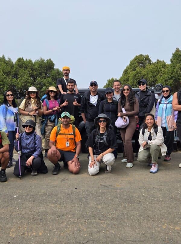Group of diverse hikers outdoors near trees and a car on a clear day.